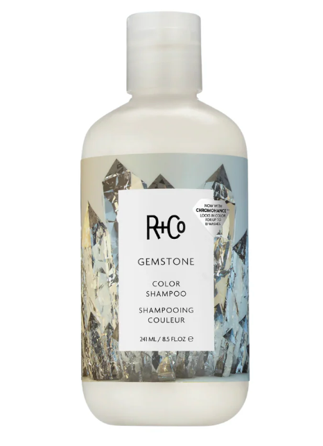 A bottle of R+Co Gemstone Color Shampoo on a plain white background. The bottle is frosted white with a label featuring a gray and white crystal mountain design.