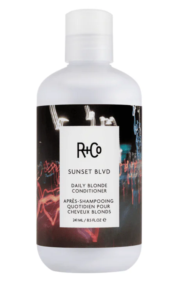 A 240 mL bottle of R+Co Sunset Blvd Daily Blonde Conditioner, featuring a white bottle and cap with a black label that has a white central label and colorful abstract light reflections.